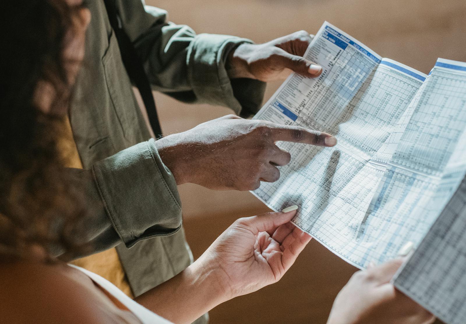 From above of crop unrecognizable black man showing paper with tables to woman in daytime